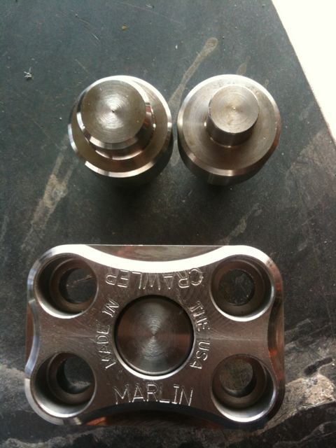 Suzuki Samurai - Close-up of metal automotive parts, including a plate stamped with 'Marlin Crawler' and two cylindrical caps.