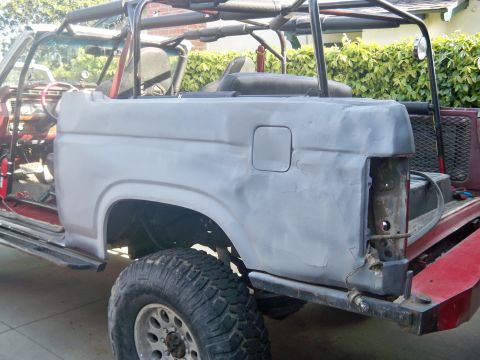 1985 Ford Bronco - A gray Ford Bronco is shown with its rear quarter panel removed, revealing the interior and a large off-road tire.