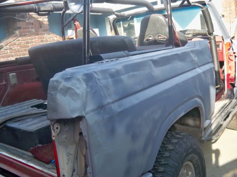 1985 Ford Bronco - The rear quarter panel of a Ford Bronco is shown with visible body damage and primer coating, indicating repair work.