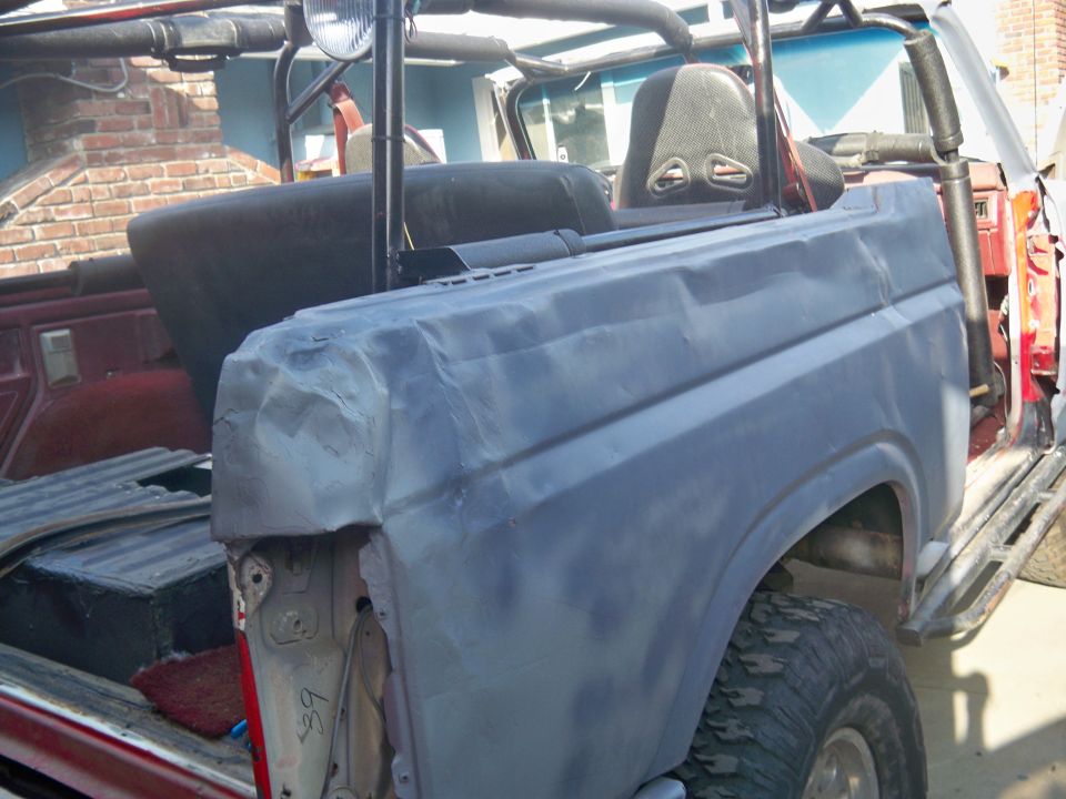 Rear quarter panel of a Ford Bronco, primed and dented, with racing seats visible inside