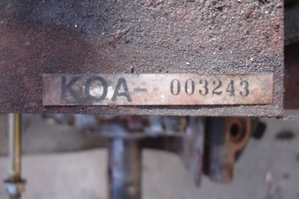 Metal plate with text KOA-003243 attached to a dirty, rusty surface