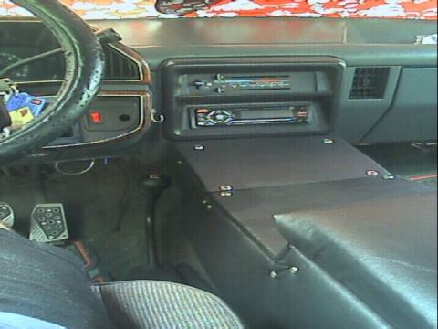 1989 Ford Bronco - Interior shot across a dark truck cab showing a homemade flat center console panel screwed over the transmission tunnel and hump, with a he…