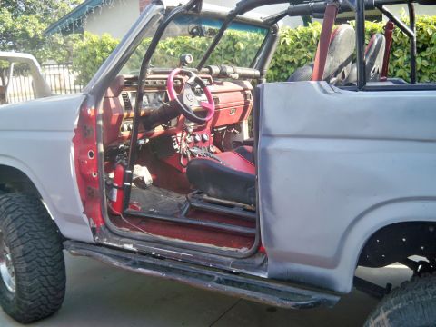 1985 Ford Bronco - This modified Ford Bronco shows its red interior and roll cage, with the driver's door removed for access.