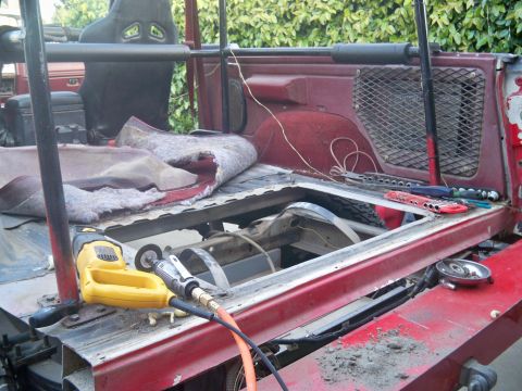 1985 Ford Bronco - Tools are laid out on the exposed frame of a red vehicle during a repair project, with the interior carpet pulled back.