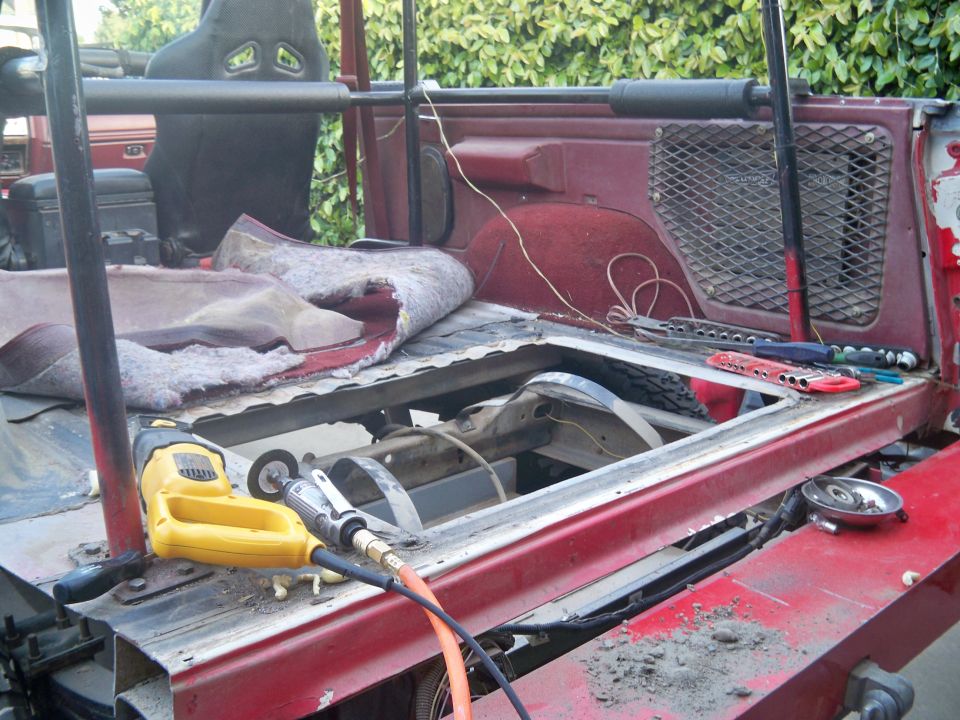 Interior of red vehicle with carpet removed, showing repair tools and exposed frame