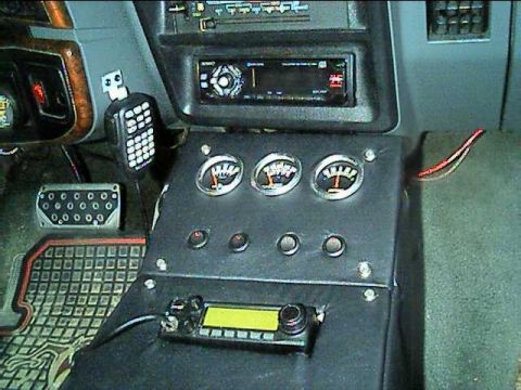 1989 Ford Bronco - Interior view of a custom center console in a Ford truck, with an aftermarket head unit above a black panel holding three round auxiliary g…
