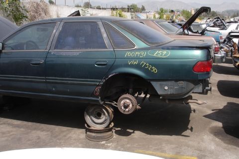 1993 Ford Taurus - A green sedan sits in a junkyard with its wheels removed and VIN 175250 visible on the rear quarter panel.