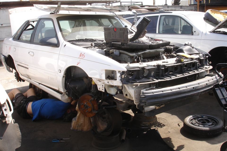 White 1993 Ford Taurus with hood open, front end disassembled, person working underneath