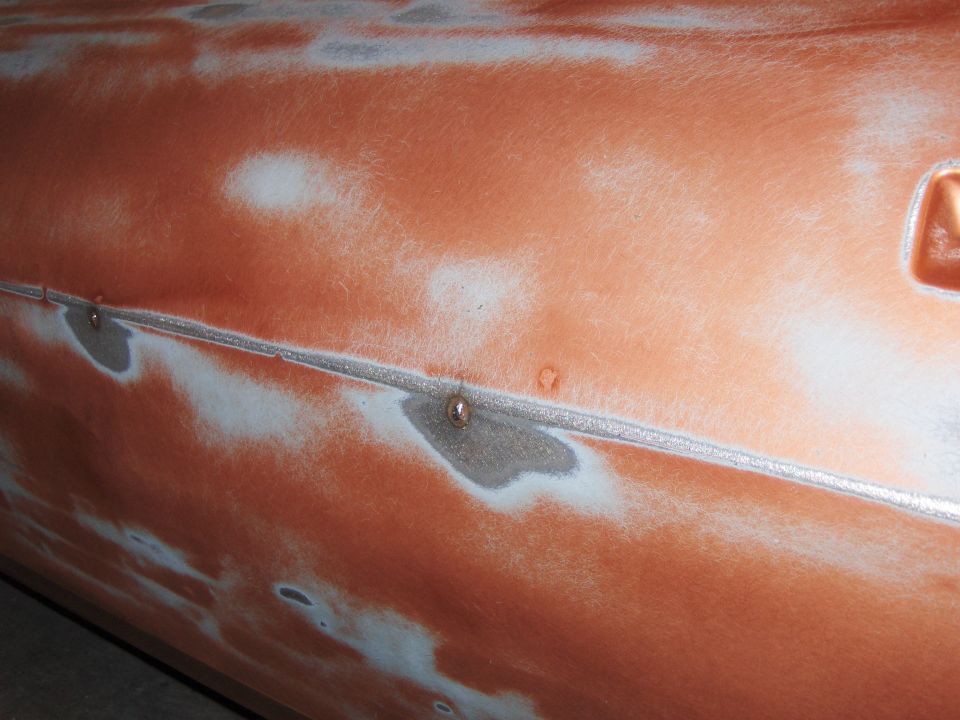 Close-up of car door showing primer and exposed metal, with a seam and rivets