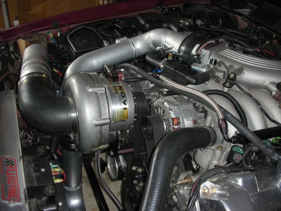 Engine bay with Novi supercharger, intercooler piping, and alternator. Fluidyne radiator sticker visible