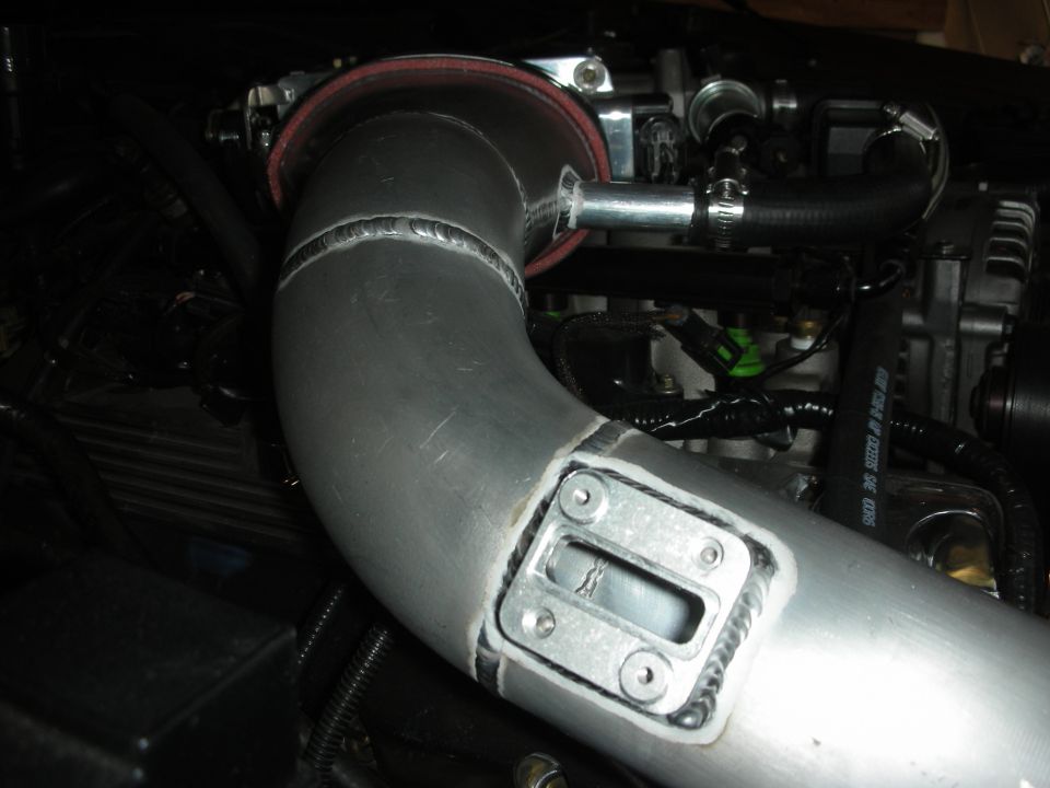 Custom aluminum intercooler piping with visible welds and a sensor mount, connected to engine components