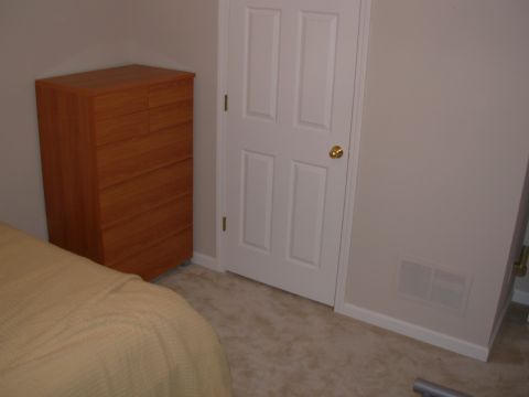 2004 Land Rover Land Rover - Interior view of a room a wooden dresser, a white door, and a bed with a tan blanket.