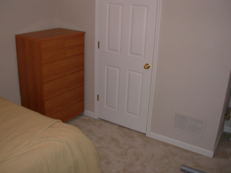 Bedroom corner with wooden chest of drawers, white panel door and beige carpet