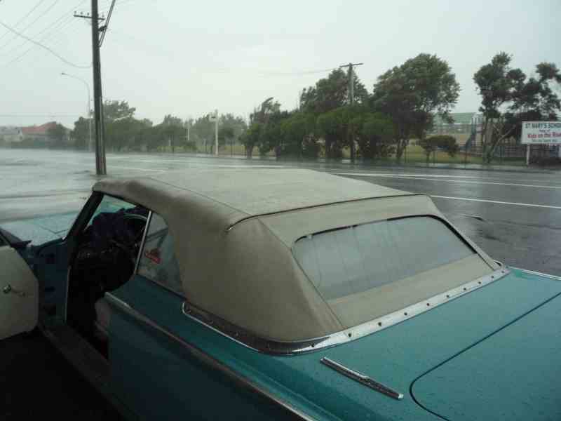 Teal 1969 Lincoln Continental convertible with tan top, driver's door open, parked on a flooded street during a storm