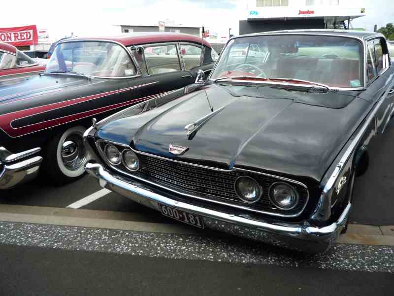 Black 1960 Ford Starliner with chrome grille and headlights, parked next to another classic car