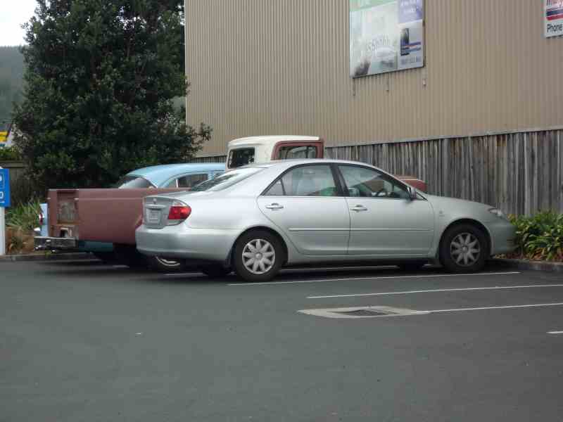 Silver sedan parked next to a rusty pickup truck with a light blue fender