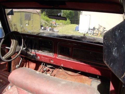1978 Ford Bronco - Interior view of a 1978 Ford Bronco shows a red dashboard and worn bench seat, with a yard visible through the windshield.