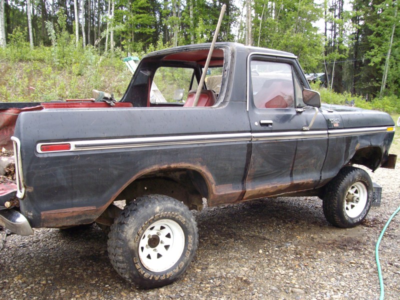 Black 1970s Ford truck with red interior and lift, side view outdoors