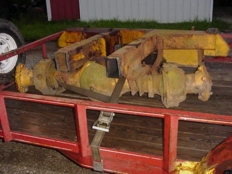 1992 Ford Bronco - A pair of heavy-duty yellow-painted axles with large center pumpkins and welded-on square-tube brackets, ratchet-strapped down to the woode…