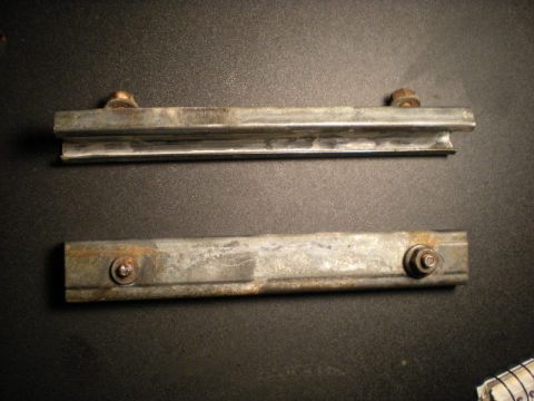 1993 Ford Bronco - Two metal brackets, likely for a tailgate, are shown with visible bolts and some rust.