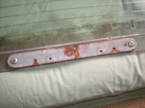 1993 Ford Bronco - A rusty tailgate bracket is shown against a green ribbed background, with visible screw holes and rivets.