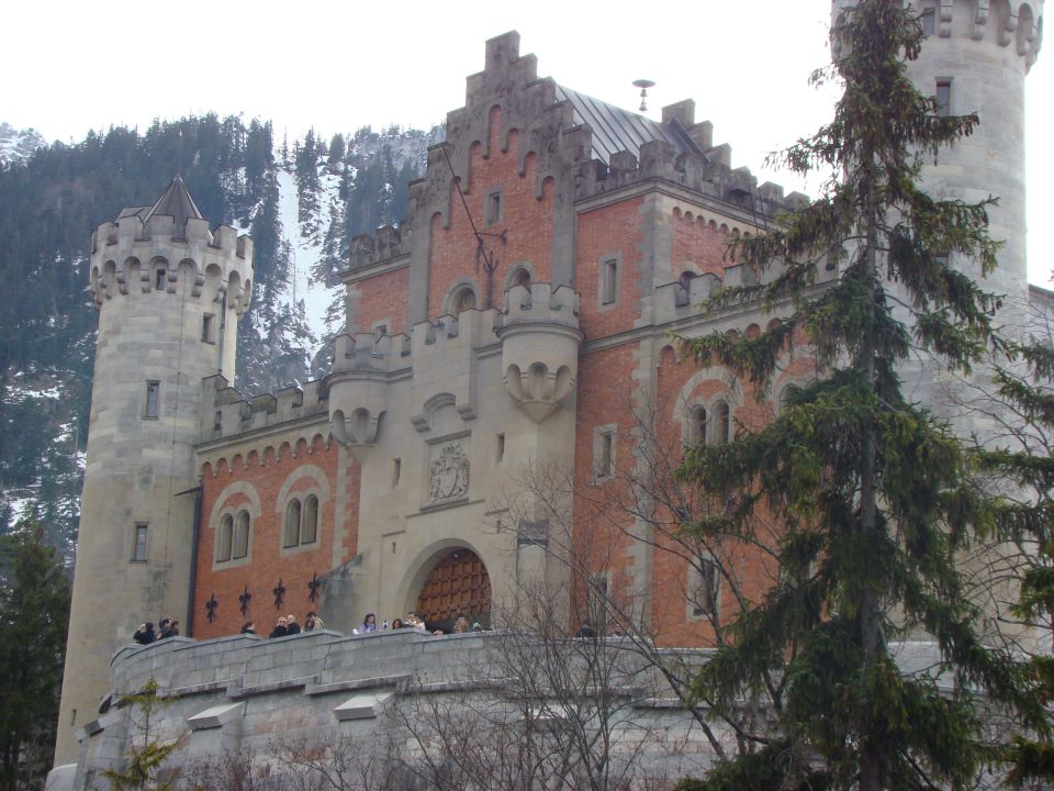 Castle with towers and red brick walls, set against a snowy mountain backdrop