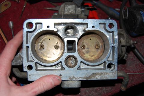 1994 Ford Bronco - A hand holds a disassembled aluminum throttle body / fuel injection unit with the upper housing removed, showing two round injector bores w…
