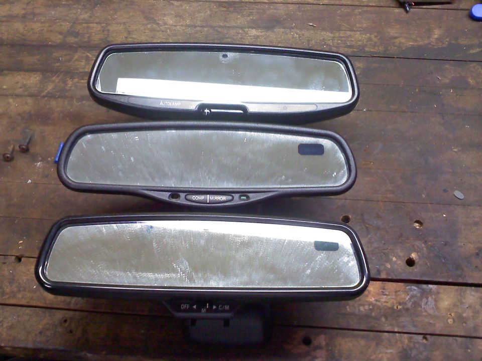 Three automotive rearview mirrors with electronic controls on a wooden surface