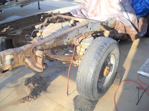 1954 Ford F-100 - The heavily rusted chassis of a truck is visible, with leaf springs and a single tire.
