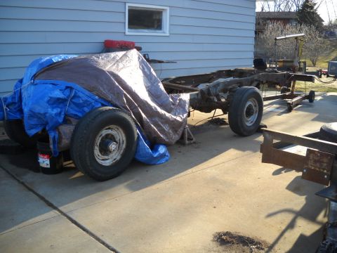1954 Ford F-100 - The chassis of a 1954 Ford F-100 pickup truck is partially covered by tarps and sits on a concrete driveway.