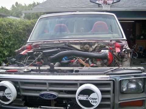1985 Ford Bronco - This 1985 Ford Bronco is undergoing engine work, with its hood removed to expose the engine bay and surrounding components.