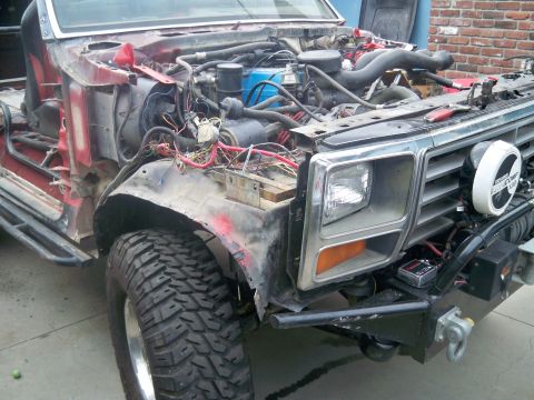 1985 Ford Bronco - Disassembled truck front end shows exposed engine and wiring, with a large off-road tire.
