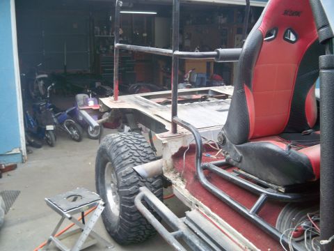 1985 Ford Bronco - Partially built tube-frame buggy with a red and black racing seat, roll cage and off-road tire under construction in a workshop.