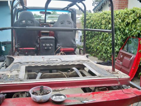 1985 Ford Bronco - Interior view of a red vehicle undergoing modification, showing bucket seats and an open bed area.