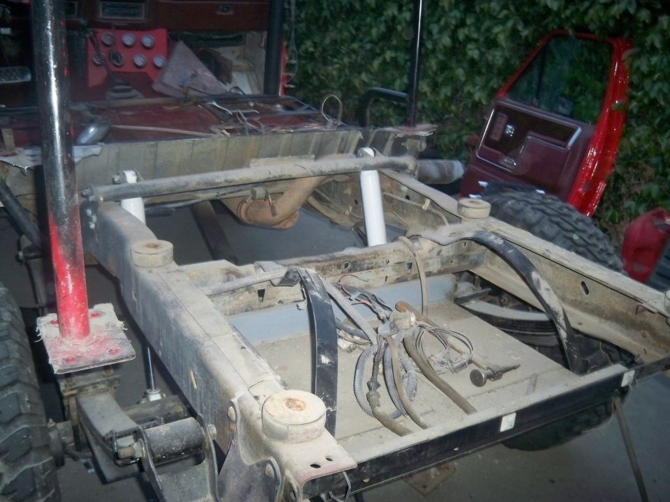 vehicle chassis with suspension components, fuel tank, and exhaust visible; red door is detached and leaning against the vehicle