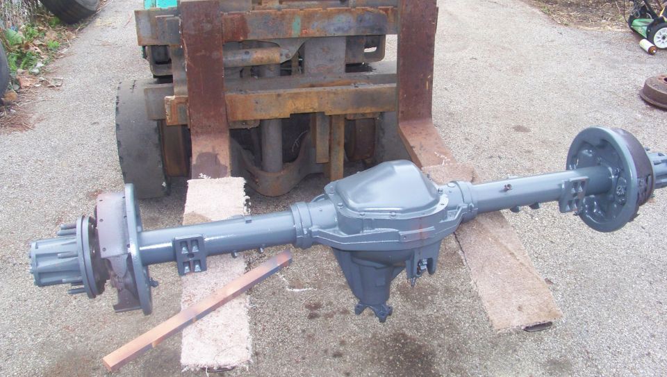 Refurbished gray rear axle assembly with differential on wood blocks in front of a forklift