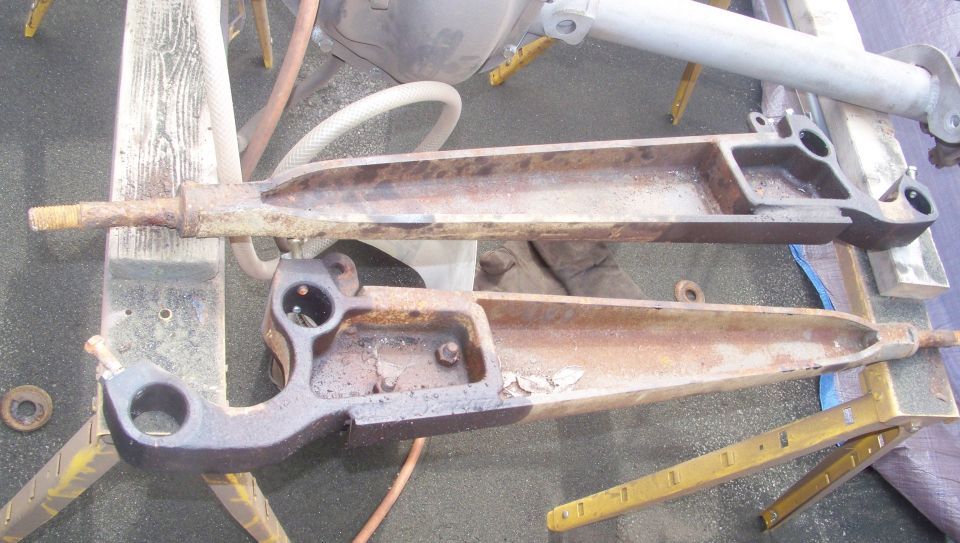 Pair of rusty radius arms removed from a truck's front suspension on a shop floor