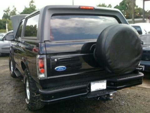 1996 Ford Bronco - Rear view of a black Ford Bronco, showing its spare tire and a partially open hood.