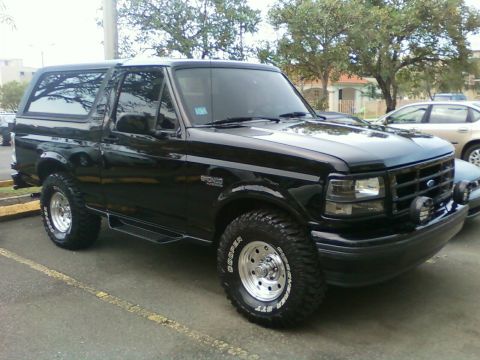 1996 Ford Bronco - A black 1996 Ford Bronco is parked on asphalt, showing its front three-quarter view with aftermarket wheels.
