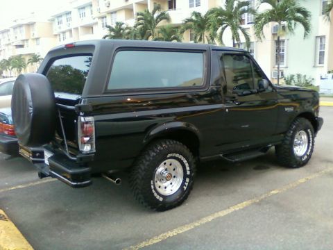 1996 Ford Bronco - This black 1996 Ford Bronco is parked in a lot with palm trees and buildings in the background.