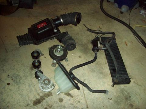 1993 Ford Crown Victoria - Various engine components laid out on a concrete floor, including an air intake system, radiator, and belt drive assembly.