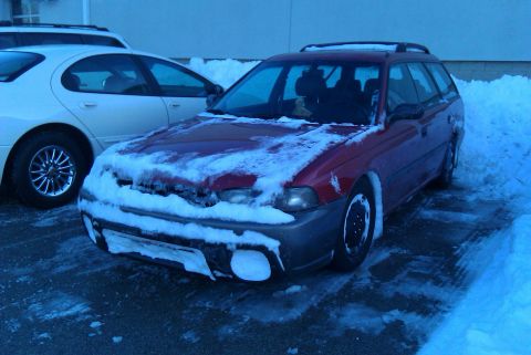 1998 Subaru Legacy - A red 1998 Subaru Legacy station wagon is partially covered in snow, parked next to another vehicle.