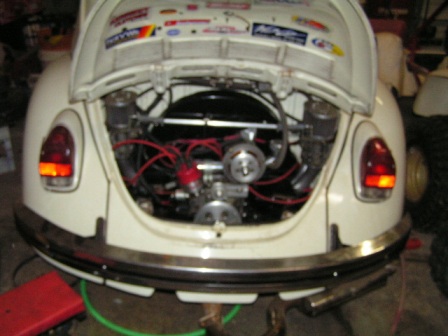 1972 Volkswagen Beetle - The rear engine compartment of a white 1972 Volkswagen Beetle is open, revealing the engine and various stickers on the lid.