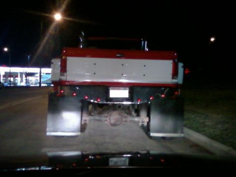 1988 Ford F-150 - The rear of a red and white pickup truck is seen at night, large mud flaps and chrome exhaust stacks.