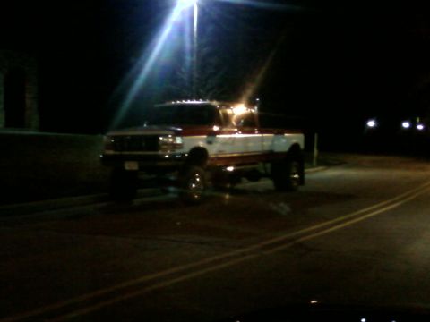 1988 Ford F-150 - A lifted two-tone pickup truck is parked on a street at night under a street light.