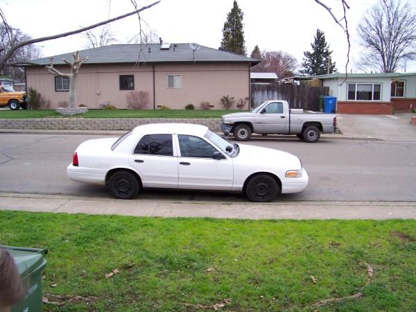 White Crown Victoria sedan with black steel wheels parked curbside on a residential street, side view