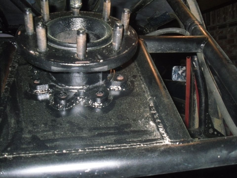 Wheel hub assembly with five studs, covered in grease, attached to a black metal frame with visible welds
