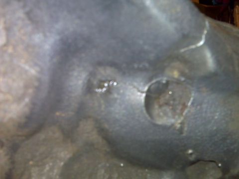 1983 Ford Bronco - A close-up view of a damaged metal component, possibly from a vehicle, shows a significant crack and a circular opening. The Supermotors.ne…