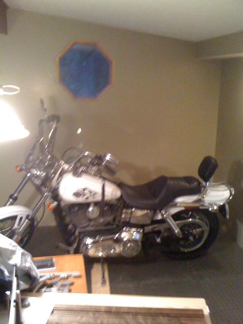 1984 Ford Bronco - A white motorcycle is parked inside a room with tan walls and a blue octagonal decoration on the wall.