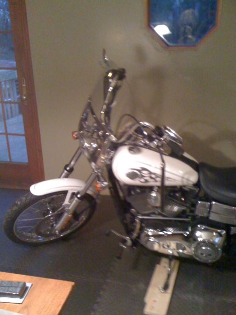 1984 Ford Bronco - A white motorcycle with flame decals is parked indoors, resting on wooden blocks.